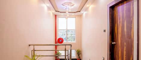 Un hall d’hôtel moderne avec un escalier, des plantes en pot, une porte en bois et une grande fenêtre.