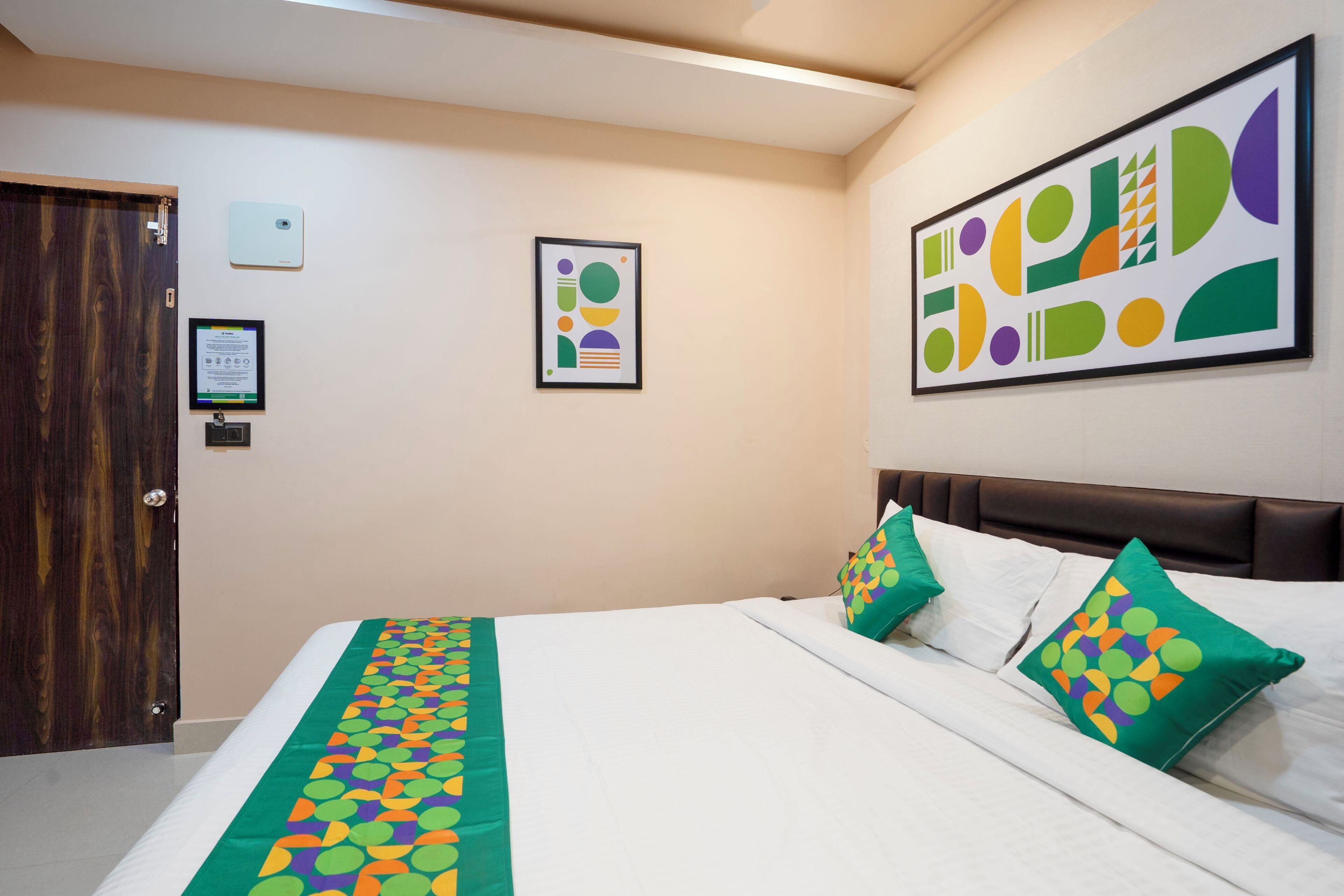 Ein Hotelzimmer mit einem Bett, einer Holztür und einem gerahmten abstrakten Gemälde an der Wand.