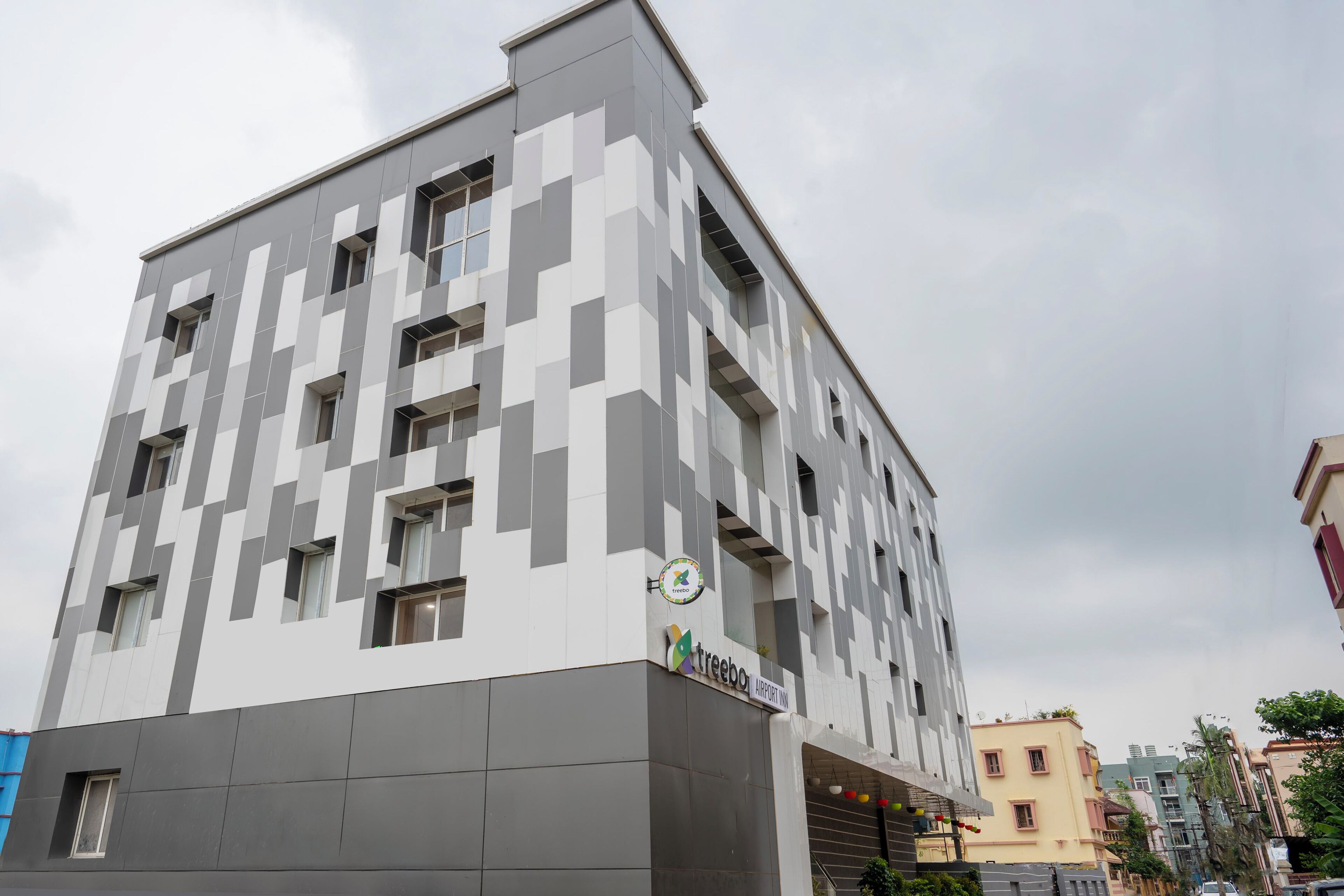 A modern building with a geometric facade, a clock, and a sign for 'Treebo Airport Inn'.