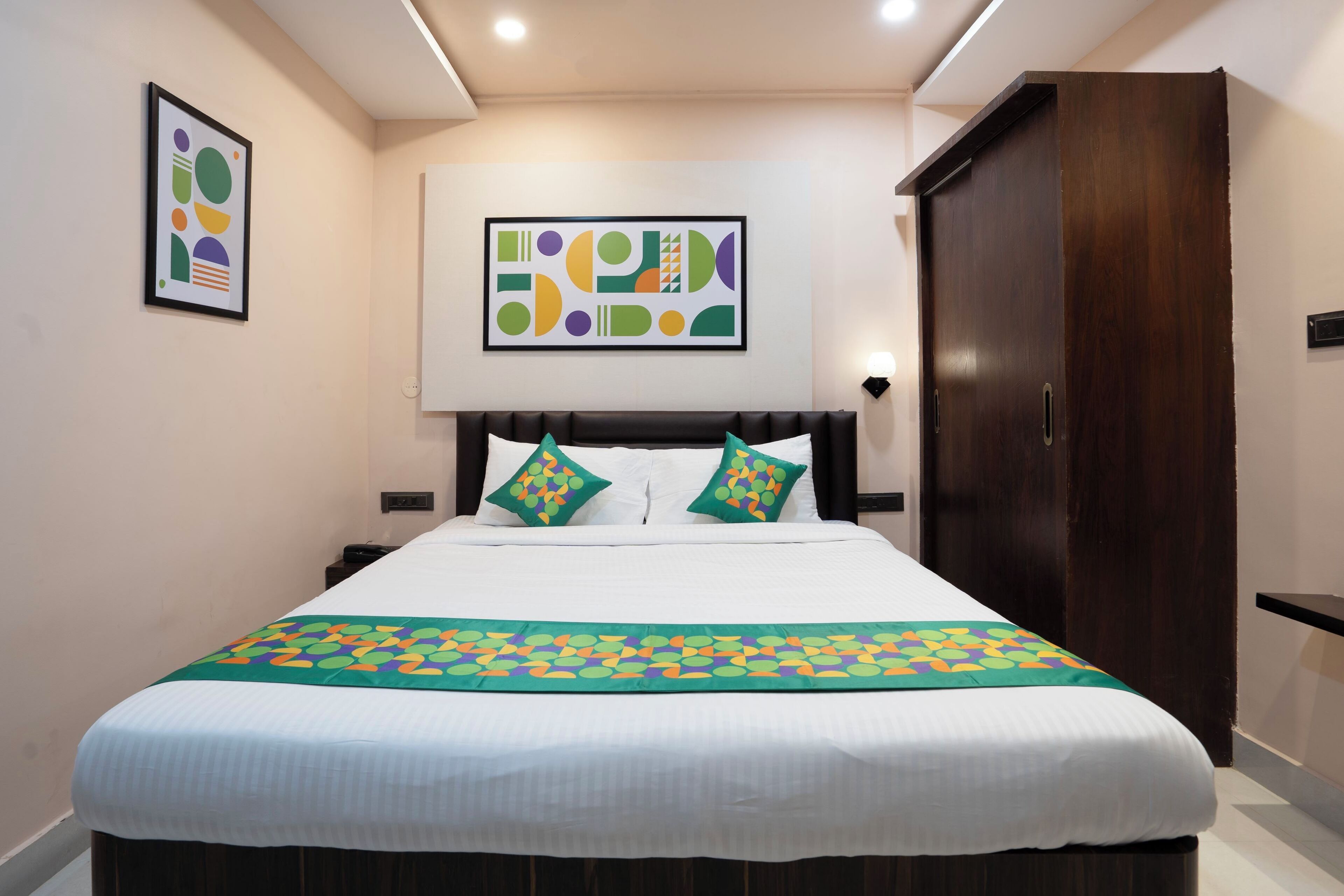 Una cama bien hecha con colcha verde y blanca, dos almohadas y un cuadro abstracto enmarcado en la pared.