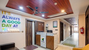 Un'area di accoglienza con soffitto in legno, una reception, un angolo salotto con sedute e un cartello con la scritta "It's always a good day at Treebo".