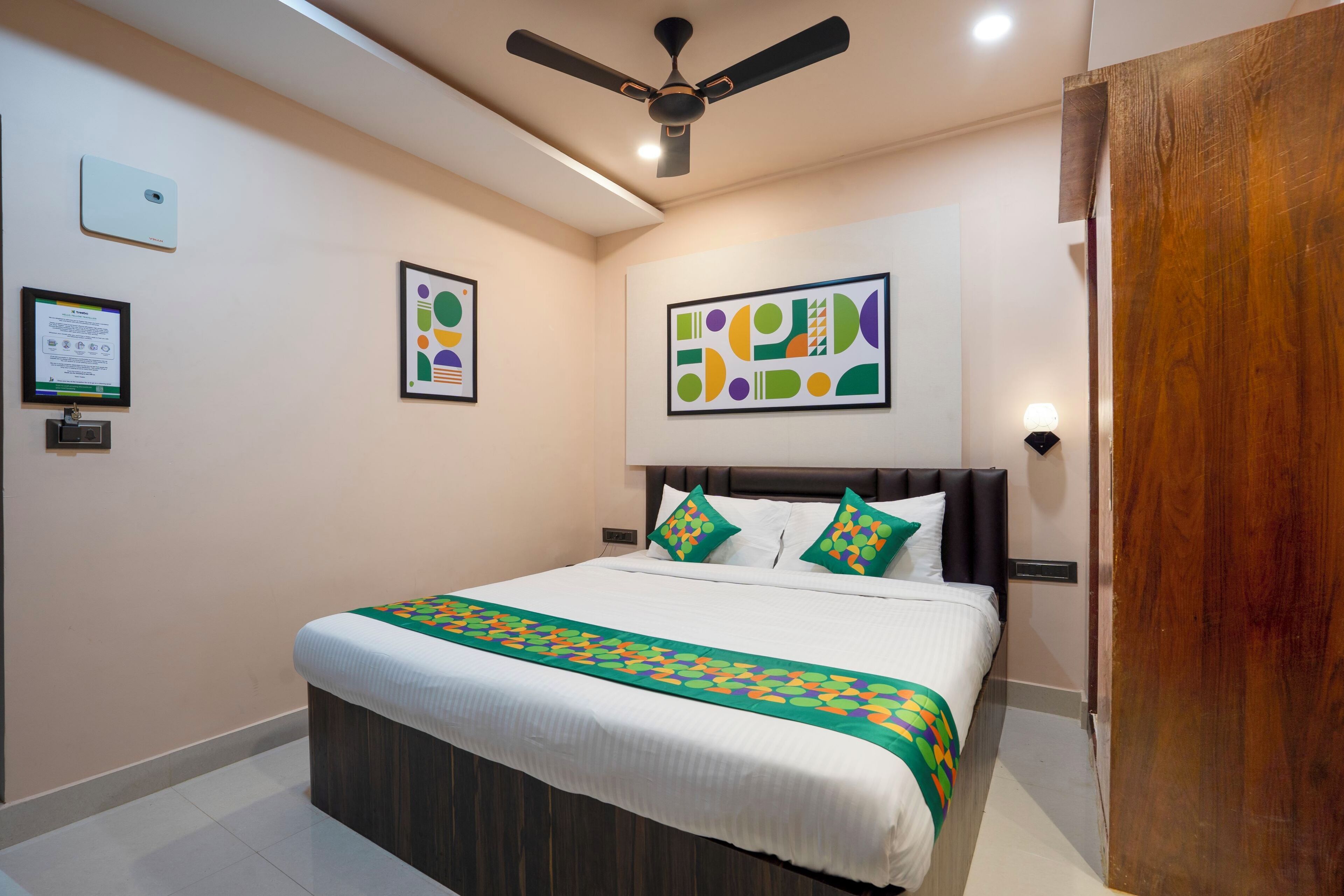 A modern hotel room with a large bed, a ceiling fan, and abstract wall art.