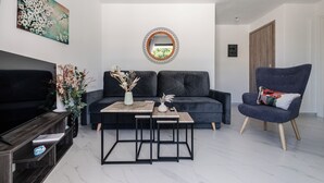 Un salon moderne avec un canapé foncé, une petite table, un téléviseur et un miroir décoratif.