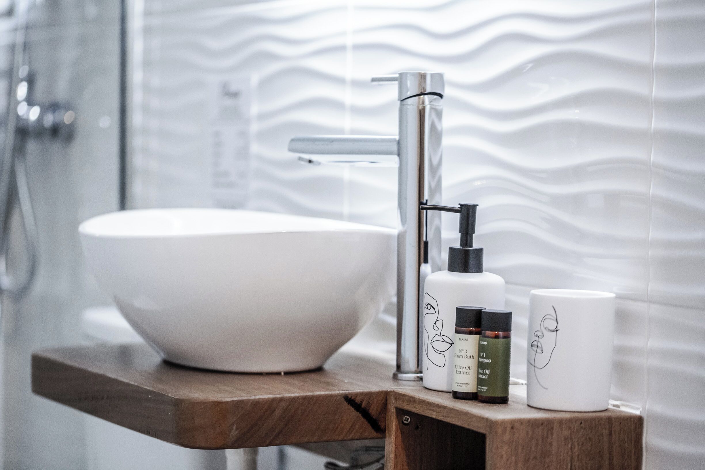 A bathroom with a white basin, a modern faucet, and a wooden shelf holding toiletries.