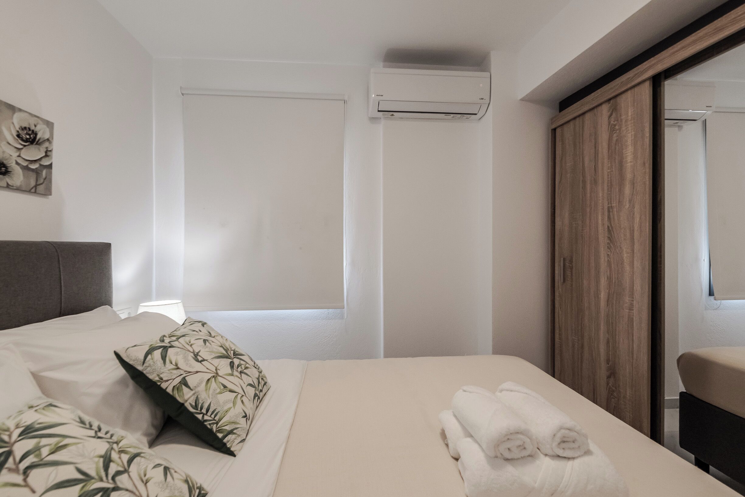 Une chambre d’hôtel comprenant un lit, une armoire en bois, un appareil de climatisation et une œuvre d’art accrochée au mur.