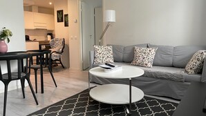 Ett modernt vardagsrum med en grå soffa, ett runt, vitt soffbord och en svartvit mönstrad matta. Det finns också en matplats med en svart stol och en rosa vas.