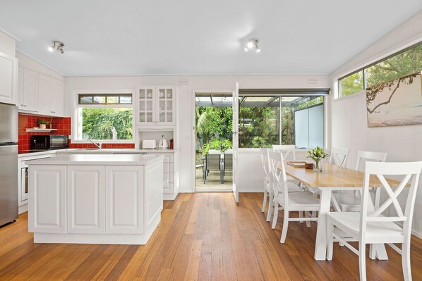 A modern kitchen with white cabinetry, a large island, and a dining area with white chairs.