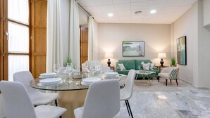 A modern dining area with a glass table, white chairs, and a green sofa in the background.