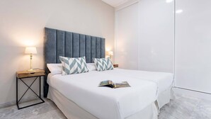 A neatly made double bed with a blue headboard, two bedside tables with lamps, and a magazine on the bed.