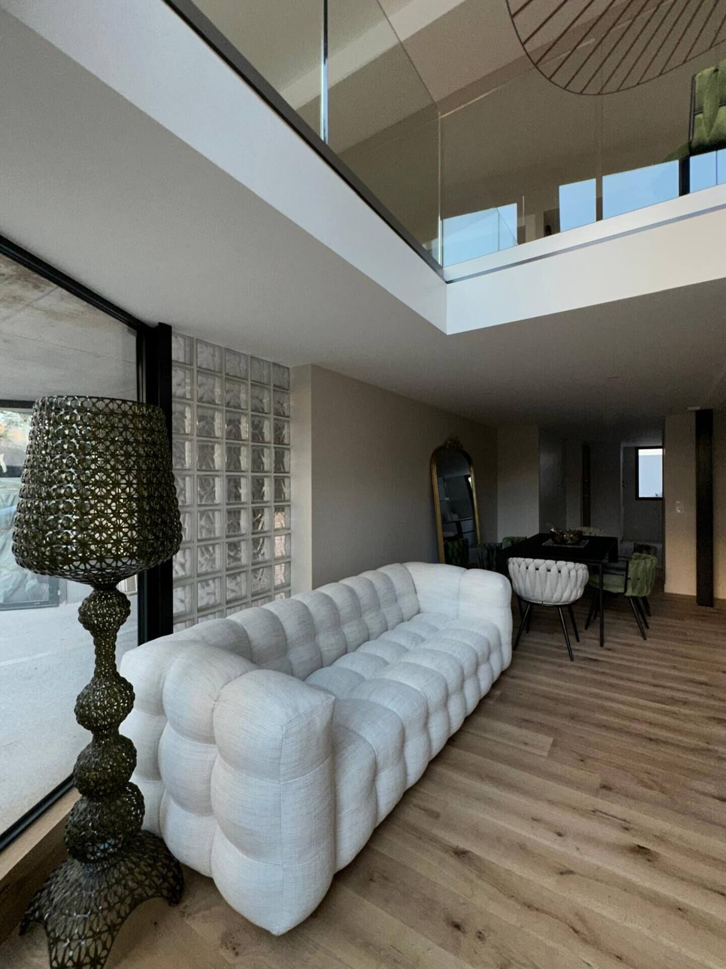 A modern living room with a white sofa, a decorative floor lamp, and a dining area with a table and chairs.