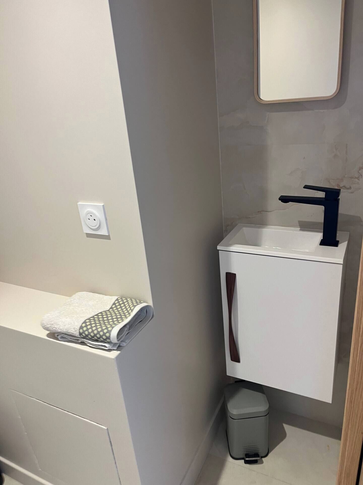A bathroom with a white sink, a mirror above it, and a towel on a shelf.