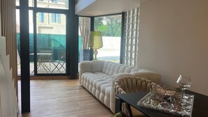 A modern living room with a sofa, a dining table with a glass top, and a view through large windows. - Nice Living Cannes Plage (Cannes)