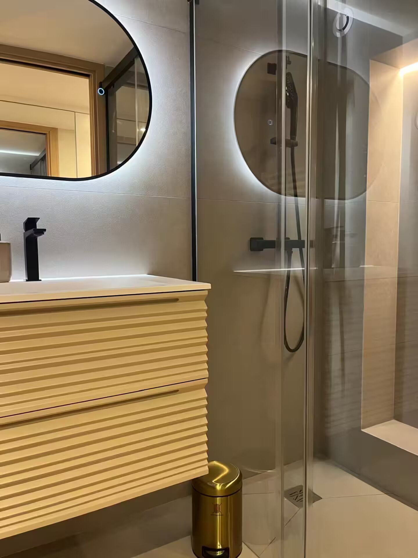 Een moderne badkamer met een houten wastafelmeubel, een ronde spiegel en een douche met glazen wanden.
