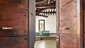 Une porte en bois donne sur une pièce où se trouvent un canapé vert et une fenêtre.