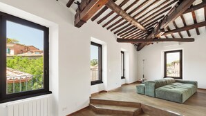 Une pièce spacieuse avec une grande fenêtre, des poutres en bois au plafond et un canapé d’angle vert.