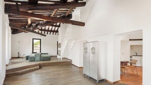 Un vaste espace de vie doté d’un plafond haut, de poutres en bois, d’un ensemble de canapés, d’un grand réfrigérateur et d’un escalier menant à un niveau supérieur.