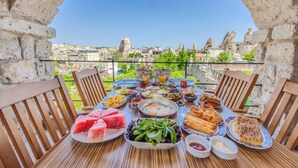 Una mesa preparada para el desayuno con diversos platos, vista a la ciudad y un arco de piedra.