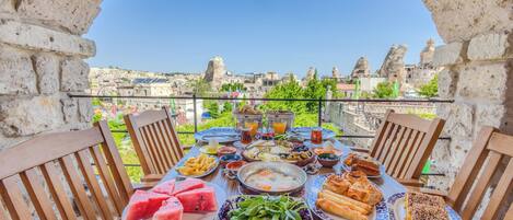 Een ontbijttafel met diverse gerechten, een stadszicht en een stenen boog.