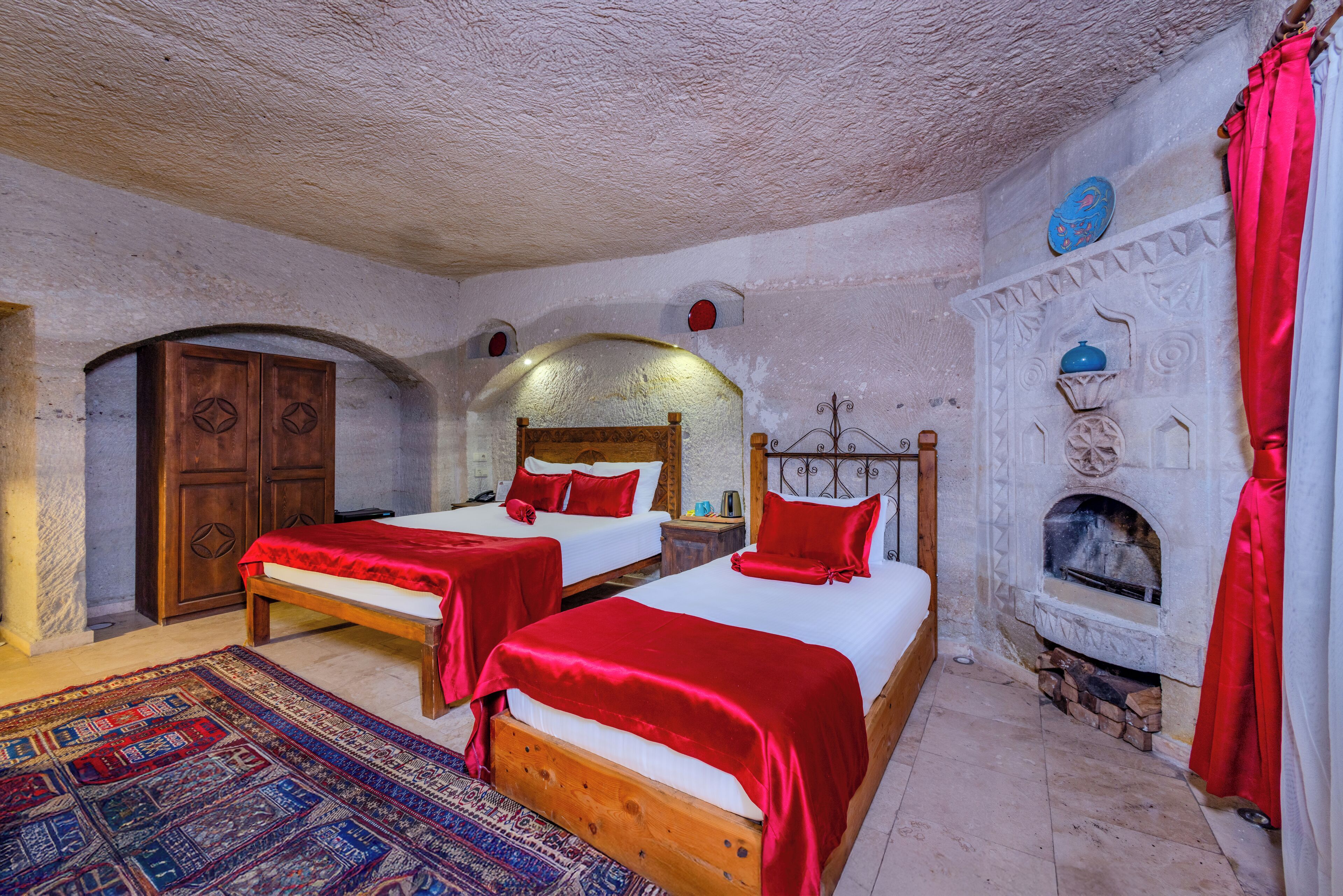 A traditional room with two wooden beds, a stone fireplace, and a carved wooden wardrobe.
