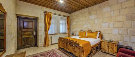 Un dormitorio con una cama de cabecera de madera, un sofá rojo, un armario de madera y una pared de piedra.