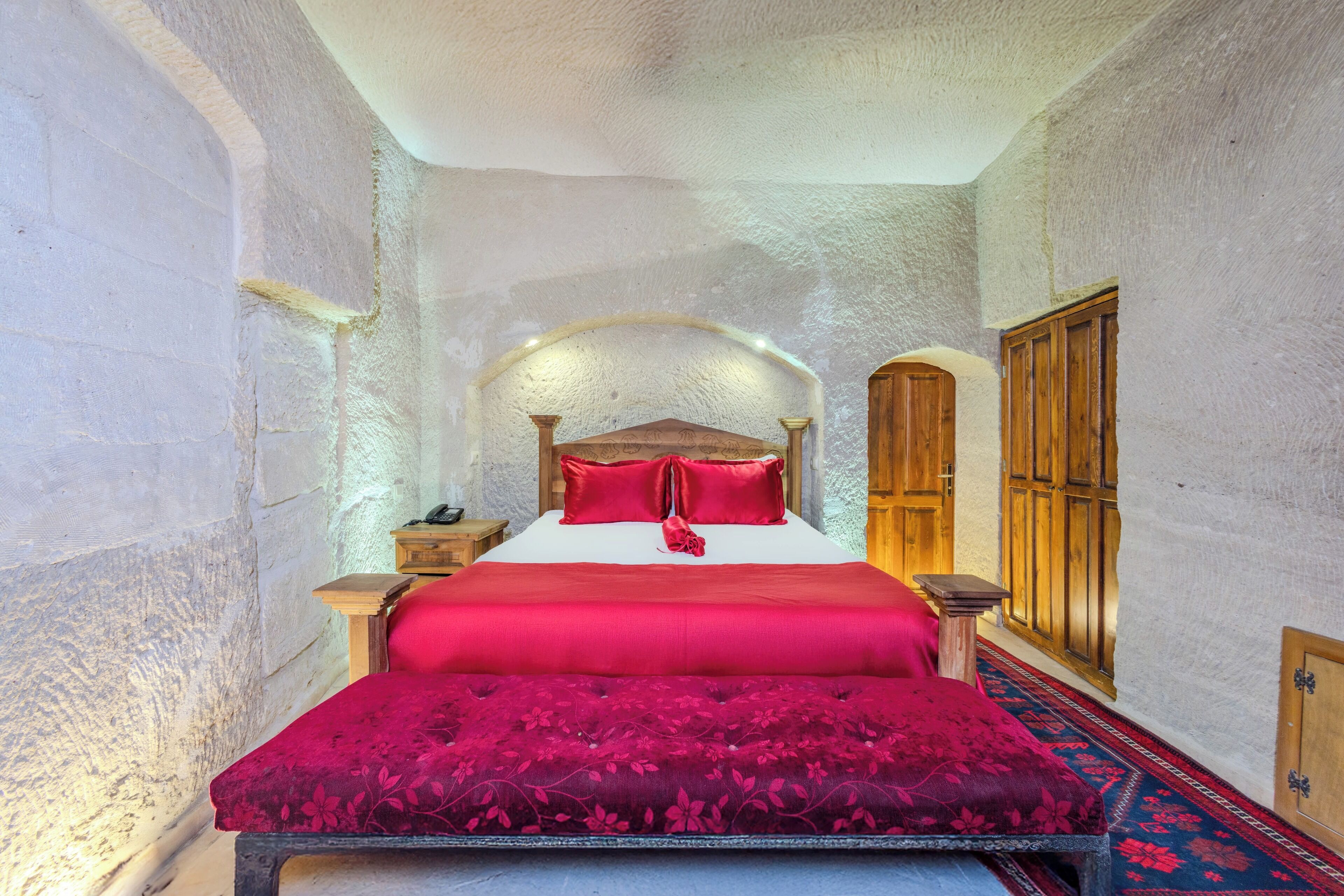 A bedroom with a large bed, wooden headboard, and a red bedspread.