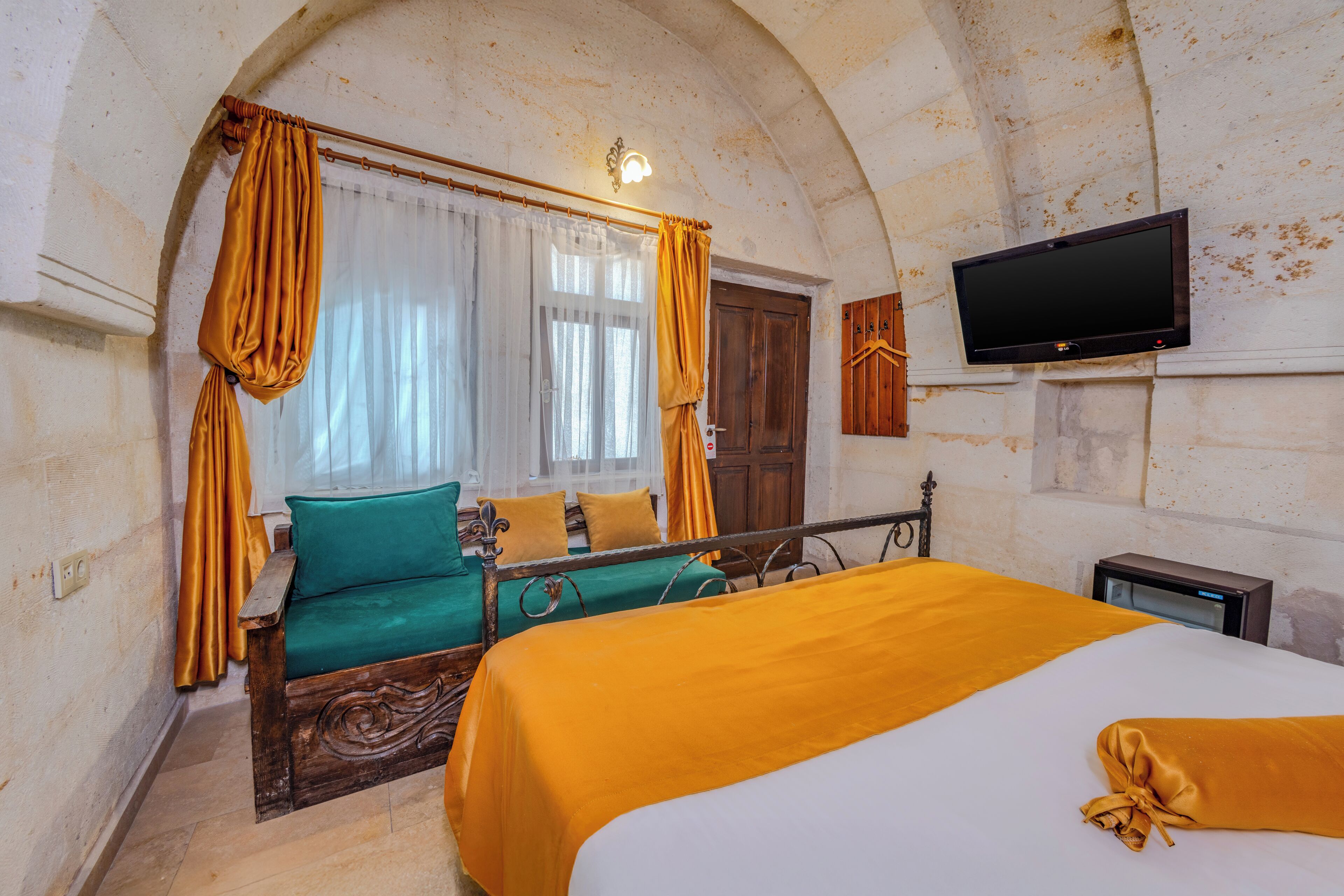 Una habitación con cama, sofá, televisión y ventana con cortinas.