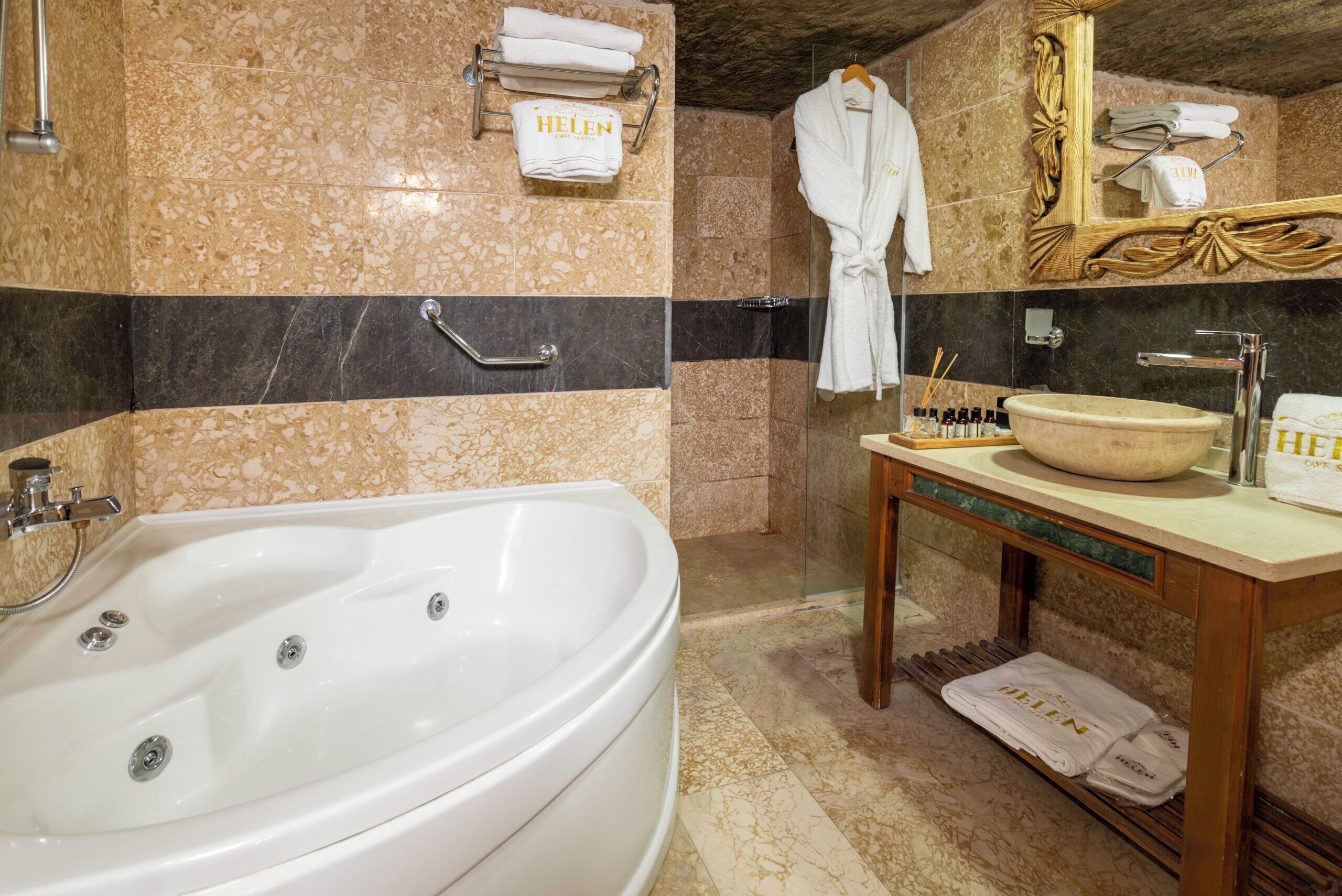 Un baño con una bañera grande, un tocador con lavamanos y un espejo. Hay toallas y artículos de aseo en el tocador.