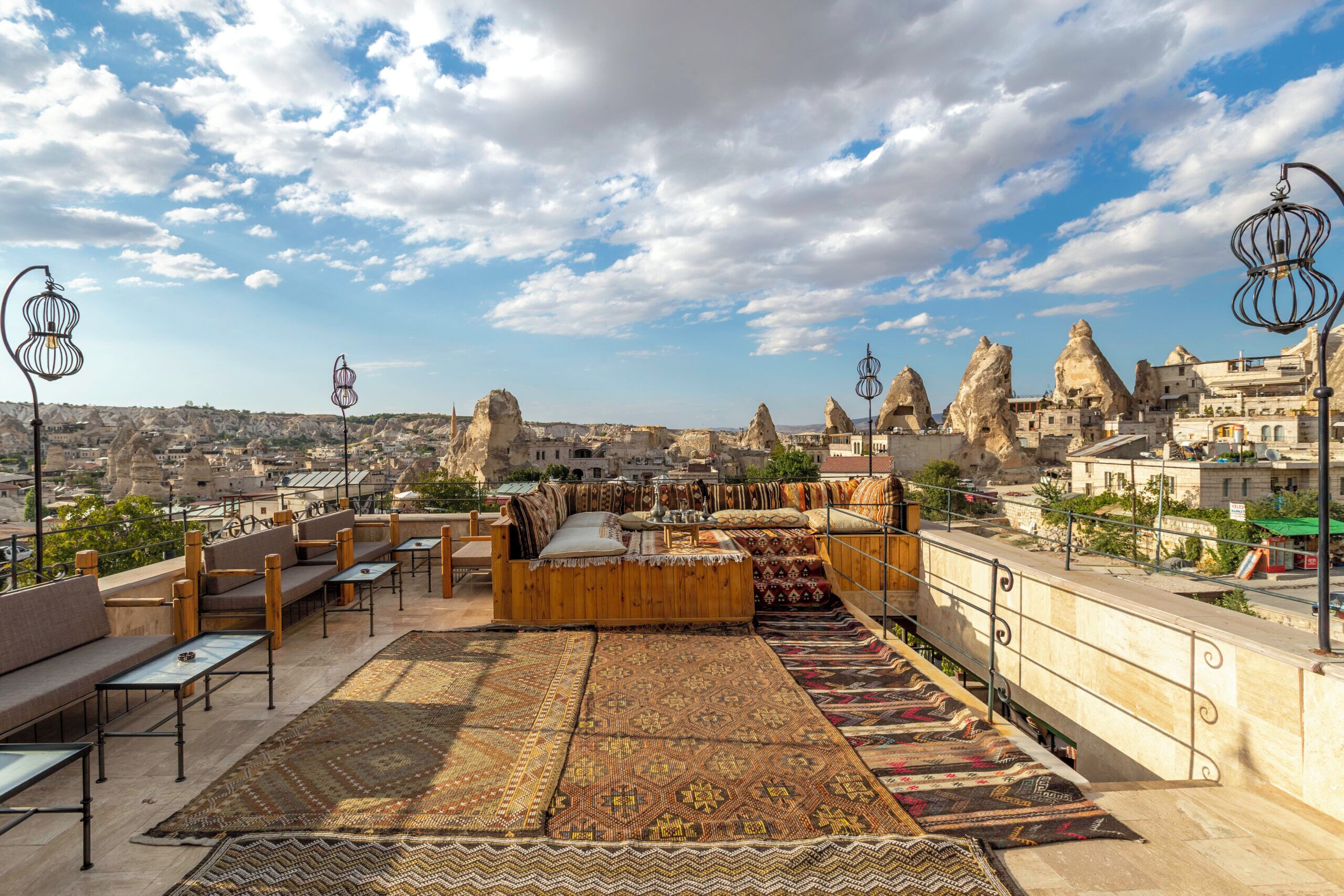 A rooftop terrace with seating, rugs, and a view of a cityscape with unique rock formations.