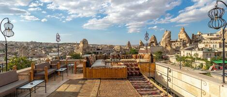 A rooftop terrace with seating, rugs, and a view of a cityscape with unique rock formations.