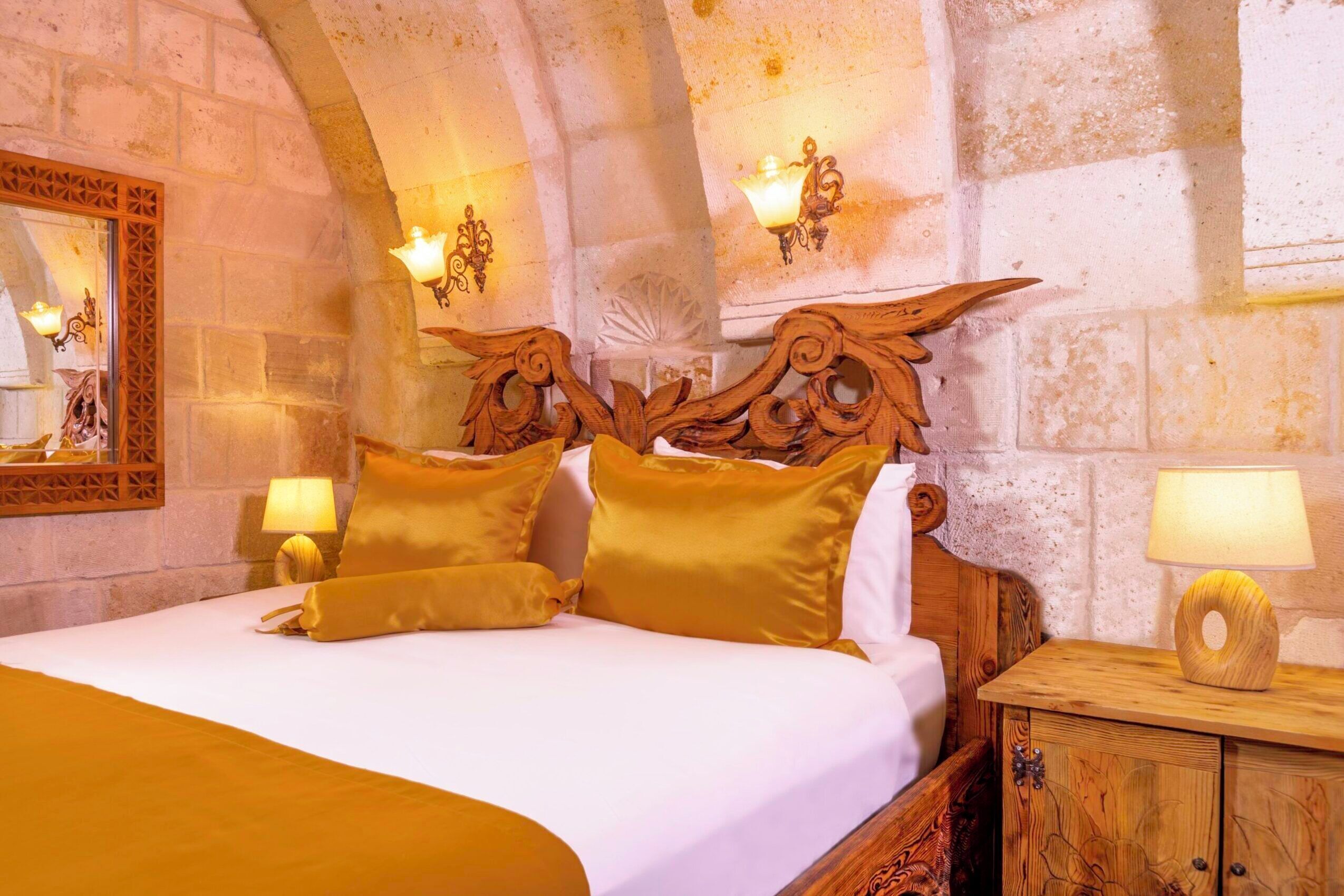 A bed with a wooden headboard, two bedside lamps, and a mirror on the wall.
