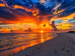 Une plage au coucher du soleil, avec un ciel dégagé et une mer calme.