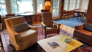 A cozy room with a large window, a wooden chair, a small table with a lamp, and a map on the table.