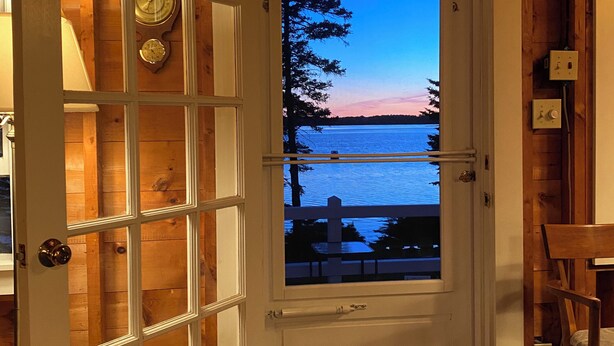 A wooden interior with a door leading to a view of a sunset over water.