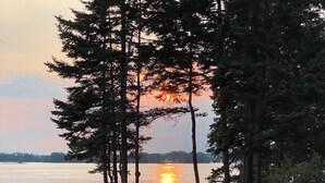 A lakeside view with a sunset, trees, and outdoor seating.
