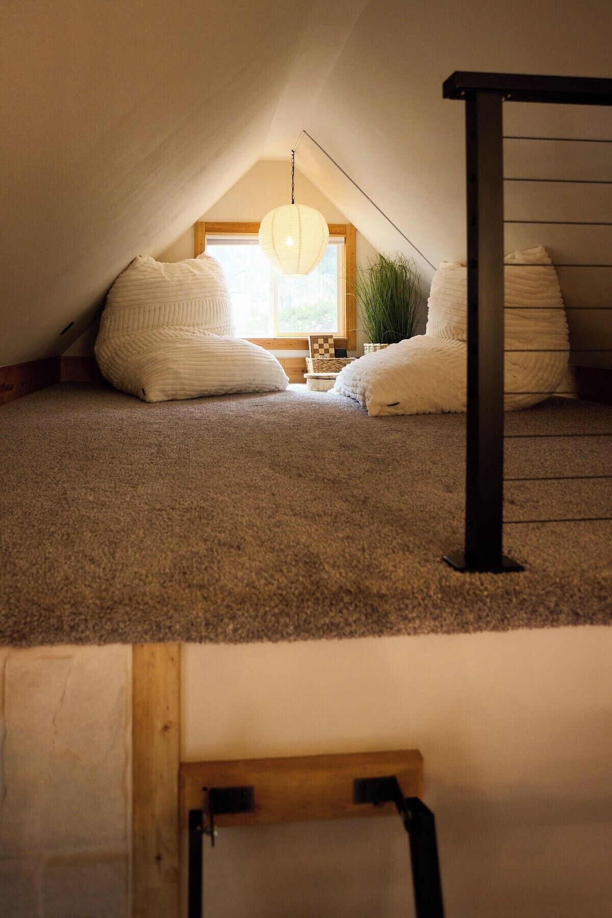 A cozy attic bedroom with a sloped ceiling, a hanging light fixture, and a view of the outdoors through a window.