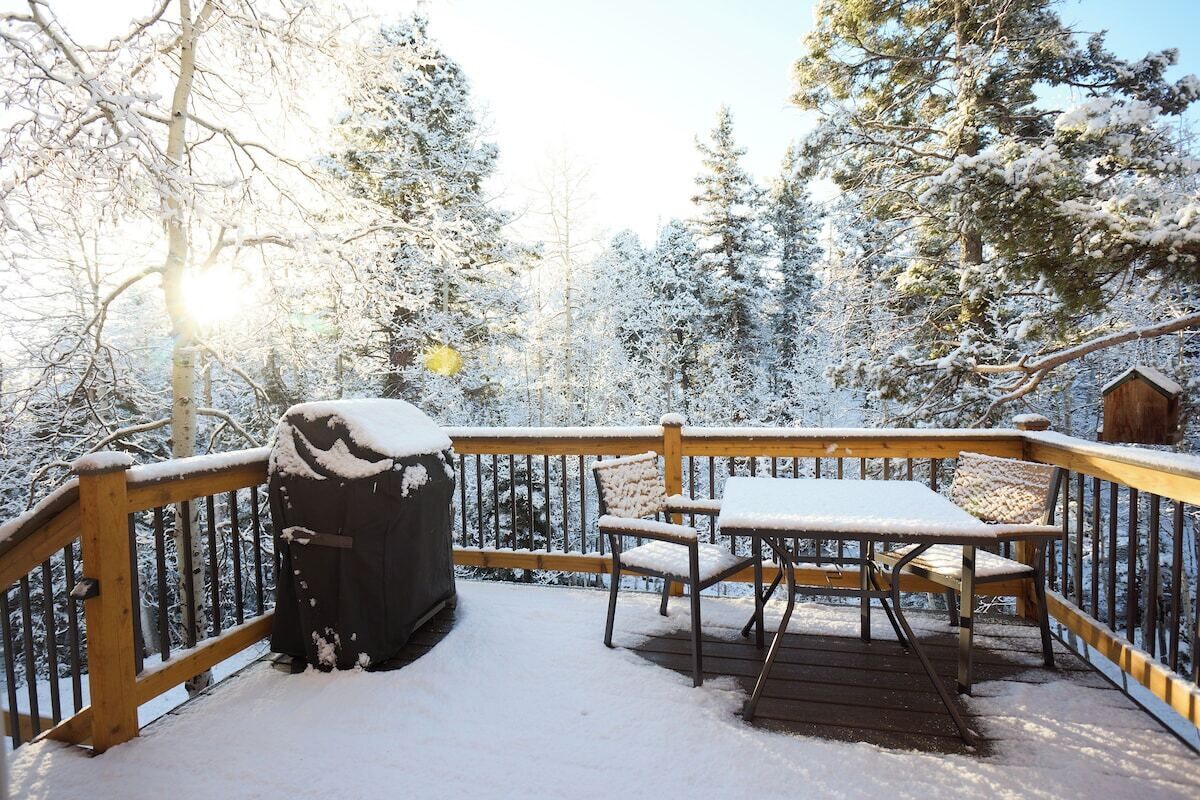A wooden deck with a table and chairs, surrounded by snow-covered trees.