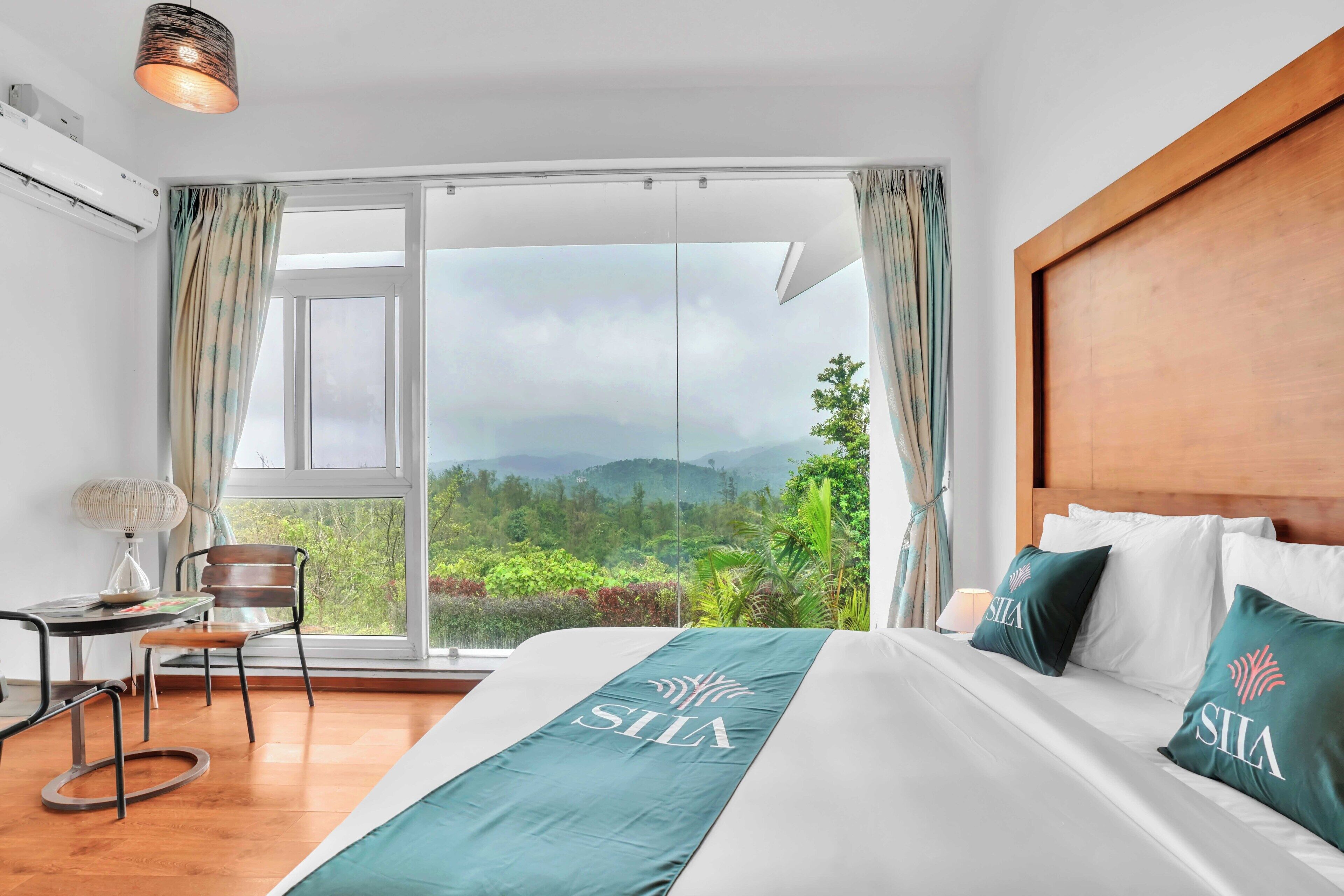 A hotel room with a large bed, a view of mountains, a wooden headboard, and a table with a chair.