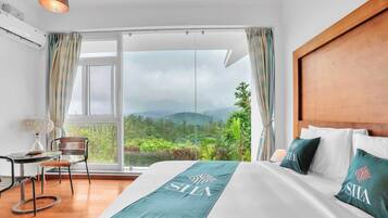 A hotel room with a large bed, a view of mountains, a wooden headboard, and a table with a chair.