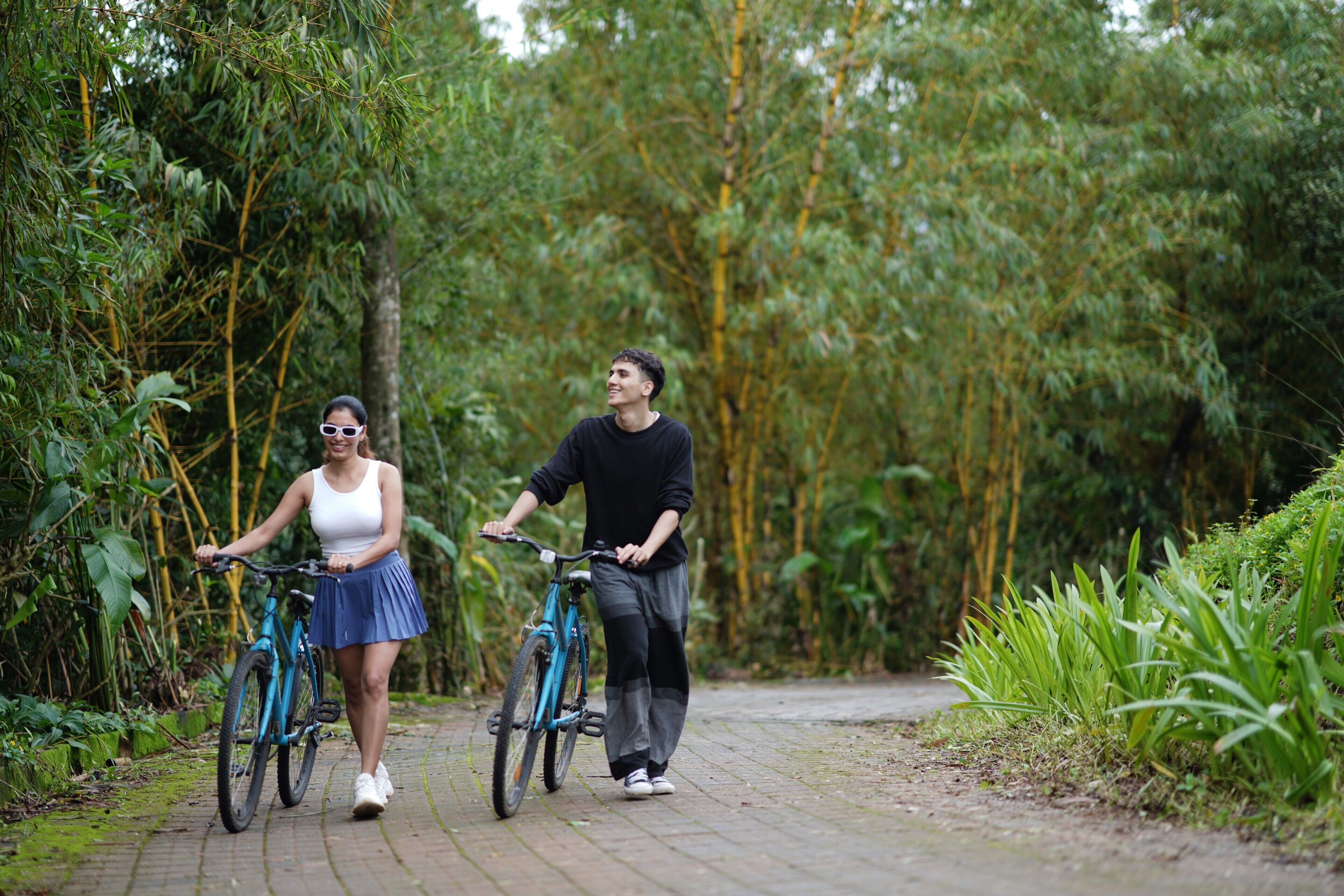 Dos personas paseando en bicicleta por un camino pavimentado, rodeado de abundante vegetación.