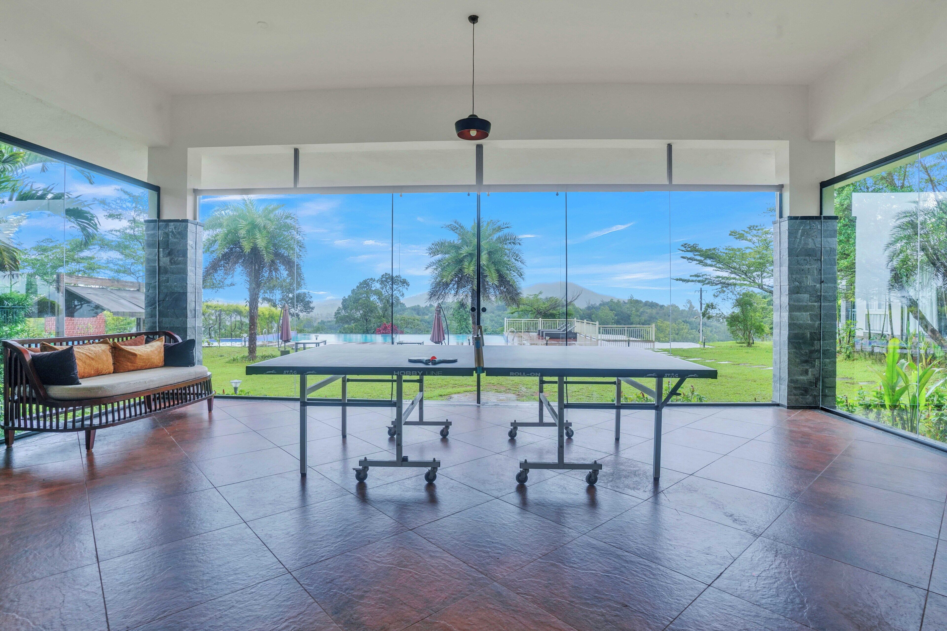 Amplia habitación con mesa de billar, sofá y ventanas grandes que ofrecen vistas a zonas verdes y una montaña distante.