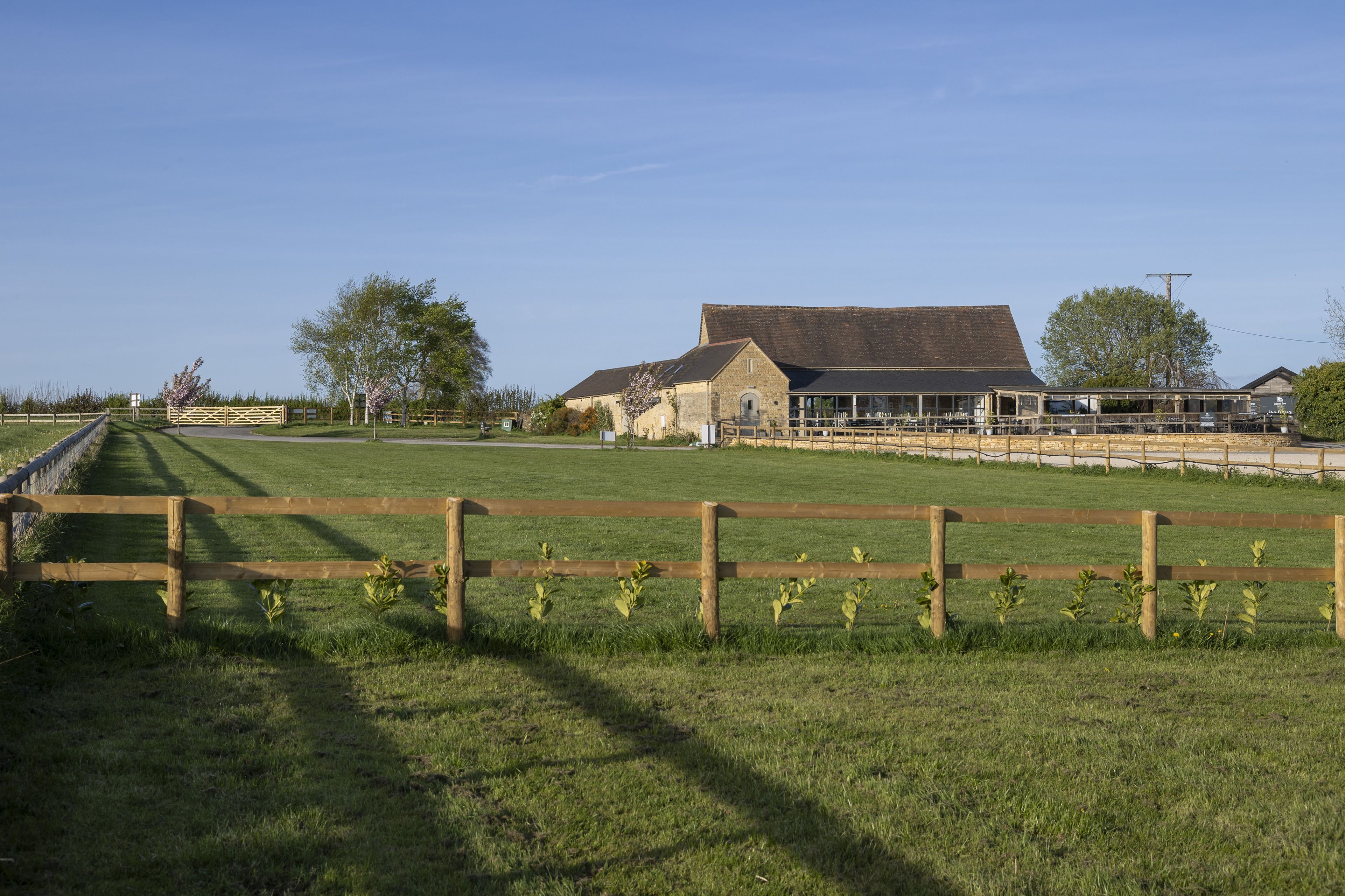 A rural landscape with a large barn, a fenced field, and a clear sky.