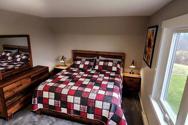 A bedroom with a wooden bed, a dresser, two bedside tables with lamps, a large window, and a painting on the wall.