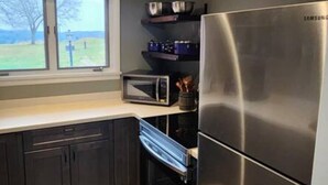 Een moderne keuken met donkere kastjes, een roestvrijstalen koelkast en een raam met uitzicht op een boom en gras.