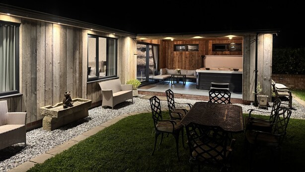 A modern outdoor living area with a hot tub, seating, and a kitchen area visible through the glass doors. - Wayside Lodge (Blackpool)