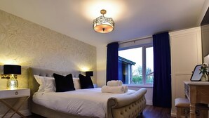 A bedroom with a large bed, a nightstand with a lamp, a dresser, and a window with curtains. - Wayside Lodge (Blackpool)
