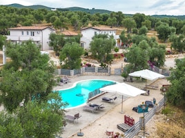 Area piscina con lettini e ombrelloni, circondata da alberi e con montagne sullo sfondo.
