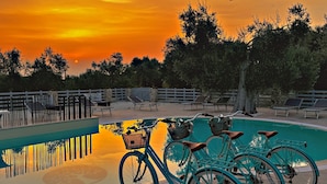 Zona junto a la piscina con vista al atardecer, una valla y varias bicicletas.