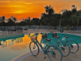 Area piscina con vista sul tramonto, una recinzione e diverse biciclette.