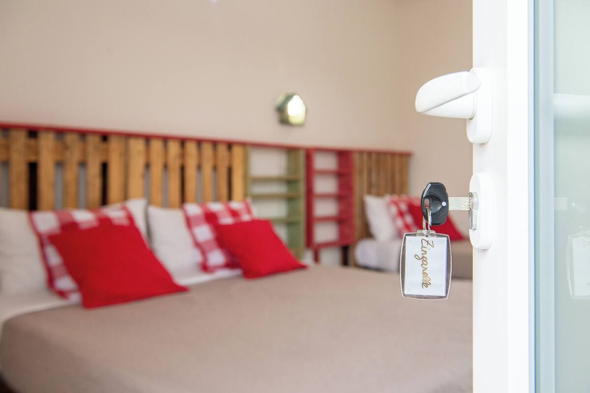 A hotel room with a bed, red and white pillows, a wooden headboard, and a key hanging on the door.