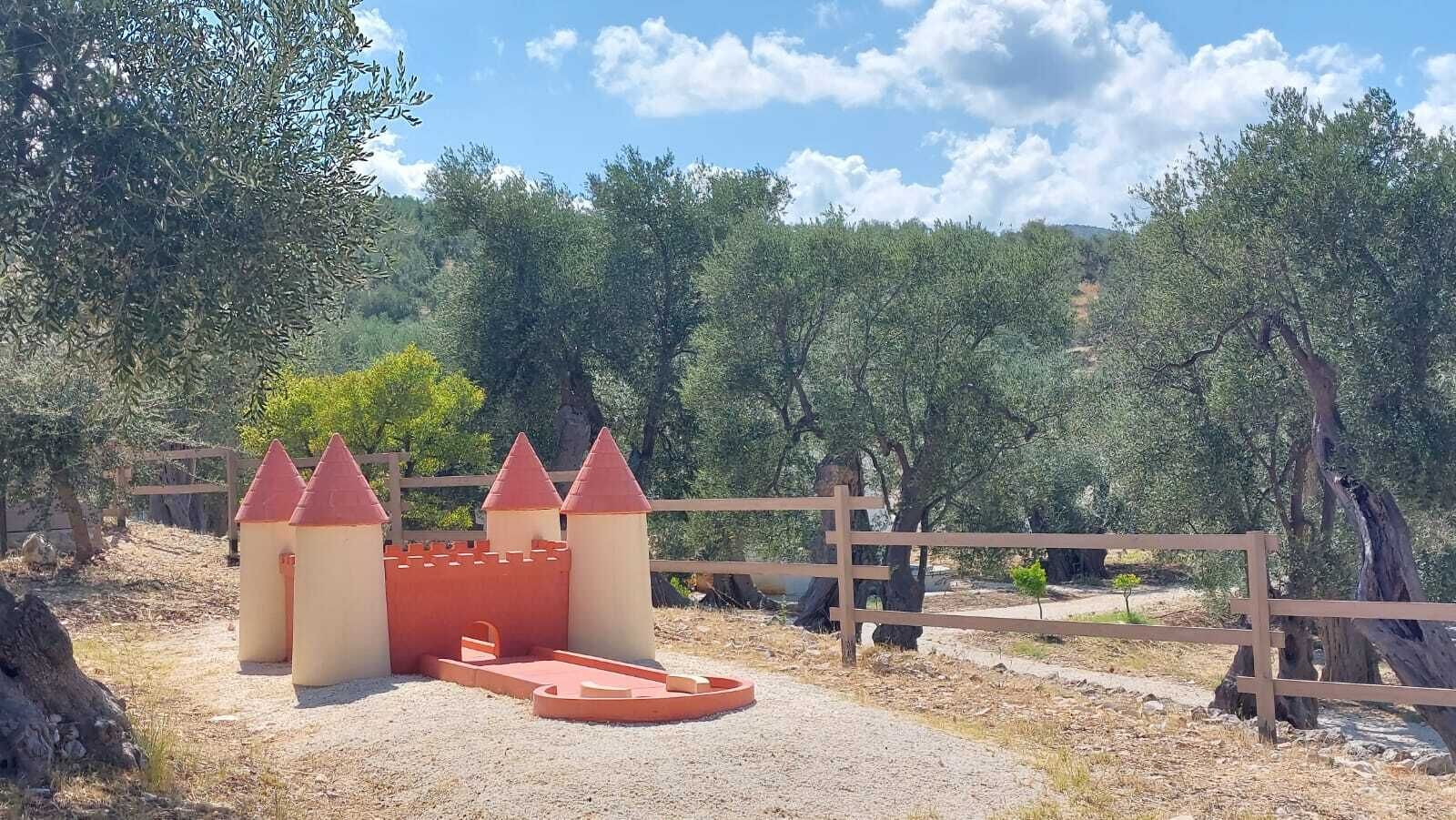 A castle-like play structure with a wooden fence and trees in the background.